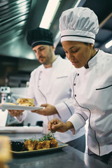 African American professional cook serving dish with her coworker in restaurant.