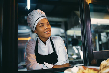 Smiling black chef looking through kitchen window.
