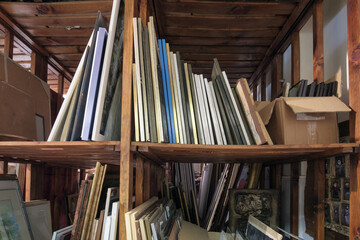 Fototapeta na wymiar Wooden shelves full of pictures, frames and art equipment. Art gallery storage