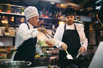 Professional cooks cooperating while preparing food in restaurant.
