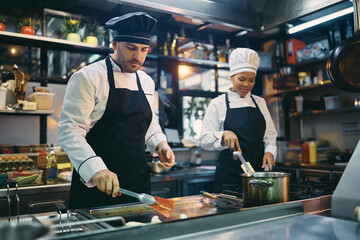 Male chef and his African American female coworker preparing food in restaurant.