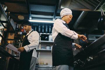 Fototapeta na wymiar Below view of happy black chef and her coworker preparing food at restaurant kitchen.