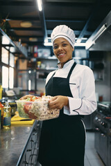 Happy African American woman works as chef at restaurant kitchen.