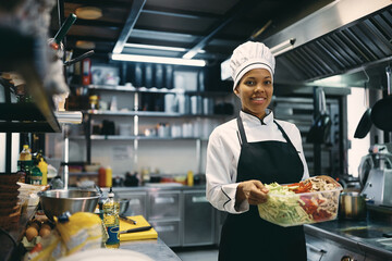 Black female chef preparing food in kitchen at restaurant and looking at camera.