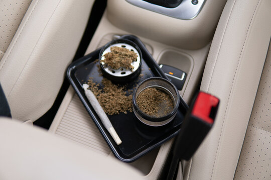 grinder and shredded cannabis joint and a packet of weed on a car background close up