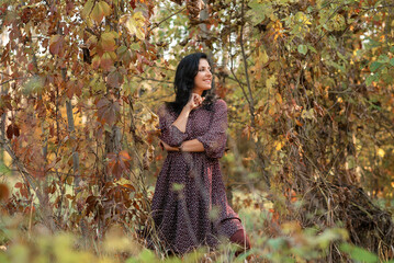 a  dark-haired woman is  standing in a beautiful autumn park