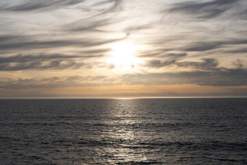 Naklejka na ściany i meble Yellow Pink Cloudy Pacific Ocean Sunset with silver gray cloudscape cold looking water below