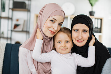 Head shot portrait happy three generations of islamic women in hijab posing for family picture,...
