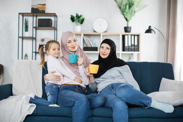 Three muslim female generations family portrait. Cute girl, islamic mom and grandma hold mugs of...