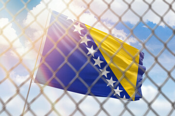A steel mesh against the background of a blue sky and a flagpole with the flag of bosnia