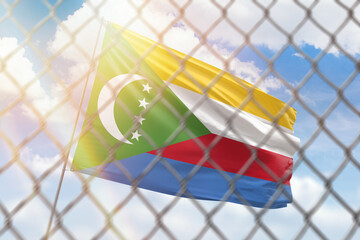 A steel mesh against the background of a blue sky and a flagpole with the flag of comoros
