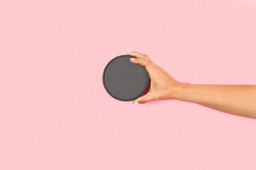 Obraz na płótnie Canvas Mano de mujer sosteniendo un tapa negra redonda sobre un fondo rosa pastel liso y aislado. Vista de frente y de cerca. Copy space