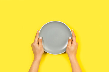 Manos de mujer sosteniendo un plato gris sobre un fondo brillante amarillo liso y aislado. Vista superior y de cerca. Copy space