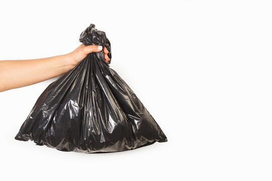 Mano de mujer sosteniendo una bolsa de plástico negra de basura sobre un fondo blanco liso y aislado. Vista de frente y de cerca. Concepto: reciclaje. Cuidado medio ambiente
