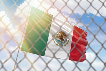 A steel mesh against the background of a blue sky and a flagpole with the flag of mexico