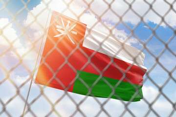 A steel mesh against the background of a blue sky and a flagpole with the flag of oman