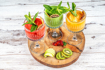 Three Fruit Smoothies or Shakes in Glasses with Strawberies,green apple and kiwi in a wooden stand.
