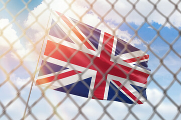 A steel mesh against the background of a blue sky and a flagpole with the flag of united kingdom