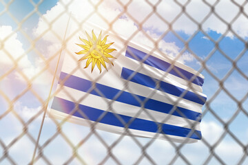 A steel mesh against the background of a blue sky and a flagpole with the flag of uruguay