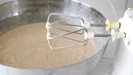 Close up of a mixer mixing pancake batter in a big silver bowl