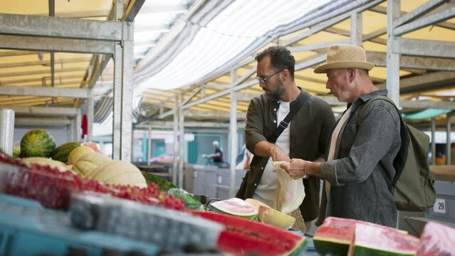 Senior man with his mature son shopping outdoors at market.
