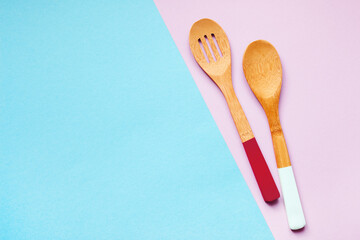 Two wooden spoons on a pink and blue background, top view, copy space.