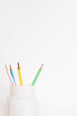 flower vase used to store some pencils, there is a blue, a pink, a green and a yellow pencil. four wooden pencils in a white glass