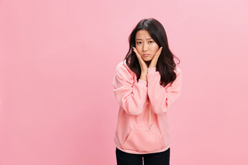 Upset unhappy cute Asian student young lady in pink hoodie sweatshirt posing isolated on over pink studio background. Good offer. Fashion New Collection concept. Copy space for ad