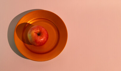 A red apple on a golden plate in a warm light. A postcard with a place for text. Top view