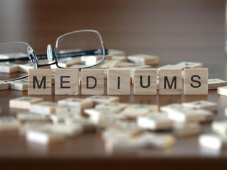 mediums word or concept represented by wooden letter tiles on a wooden table with glasses and a book