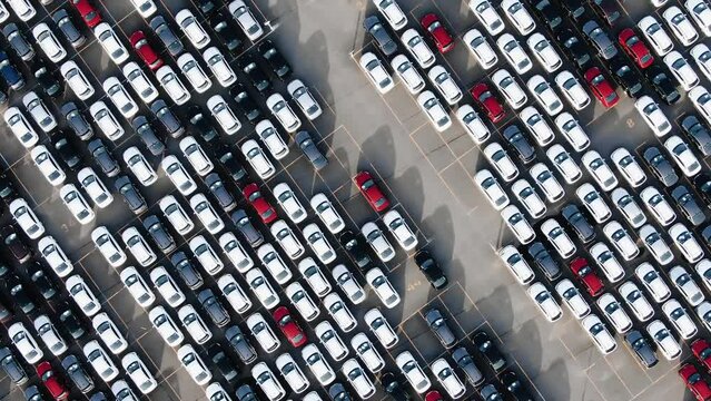 Aerial view of a giant parking lot of new multi-colored passenger cars standing in neat rows. The crisis of mechanical engineering and the violation of logistics.