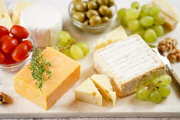 Cheese platter with organic cheeses - blue cheese cheddar, emmantaler, french soft cheese with strong smell, italian parmesan, grapes, tomatoes, olives, nuts and crackers on marble board