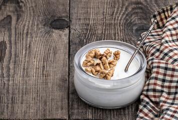 Fresh natural homemade organic yogurt with walnuts in a glass jar on wooden table