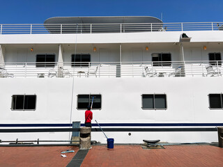 A lone maintenance worker paints the side of a cruise ship while docked in port.