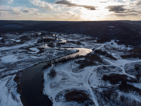 Winter aerial rural epic view on snowy river valley from drone. Zmiyevsky region on Siverskyi Donets River in Ukraine. Contrast river curve under sun in clouds