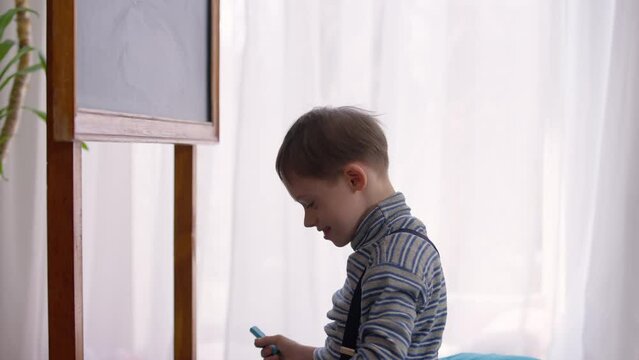 Side View Portrait Of Joyful Autistic Schoolboy Cleaning Blackboard With Cloth Indoors In Classroom. Happy Smiling Caucasian Child With Birth Anomaly Studying In School. Autism And Intelligence