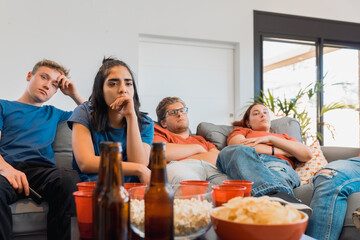 Obraz premium sad friends watching TV because their football team lost the game. upset young people at a house party.