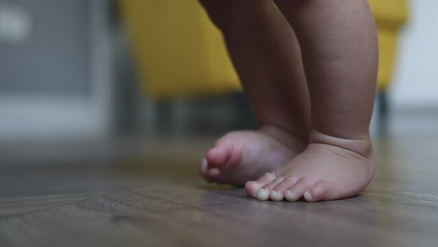 close-up baby infant feet, little foot moving fingers toes, trying to stand for the first time. baby toddler naked legs, learning to step or walk. barefoot and bare feet little children indoors floor 