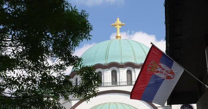 the temple of Saint Sava in Belgrade with a golden cross and the Serbian flag