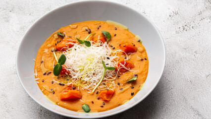 Pumpkin traditional soup with creamy silky texture, garnished with tomatoes and parmigiano. Marble background. Copy space. Top view