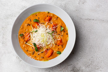 Pumpkin traditional soup with creamy silky texture, garnished with tomatoes and parmigiano. Marble background. Copy space. Top view