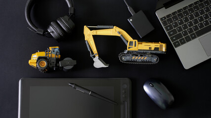 Stylus, graphics tablet, mouse, laptop, ssd drive and headphones next to models excavator and asphalt roller. Design of construction equipment and engineering of landscaping works. Workplace