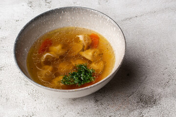 Tasty chicken soup bouillon with dumplings, chicken meat and parsley in a white bowl. Isolated on marble background. Healthy meal menu.