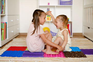 Girls play and have fun together in the children's room on the floor on orthopedic massage mats....
