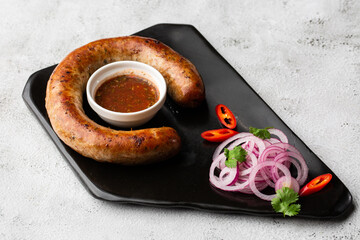 Juicy homemade baked sausage on a plate with spicy sauce and marinated onion on marble background.