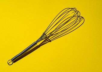 whisk on a yellow background with hard shadows