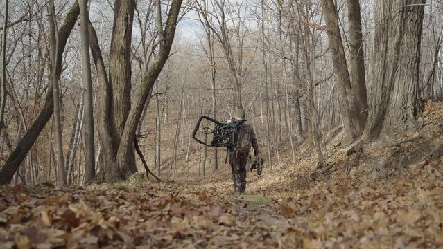 Gimbal following bowhunter in camouflage outfit walking in forest path during winter