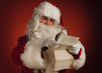 Santa Claus reading a letter with use of a Loupe - obrazy, fototapety, plakaty