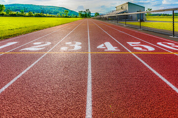 Low perspective image of new outdoor 6 lane running track start line with sun and clouds on the horizon.
