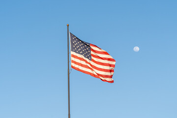 Flag of the United States waving in the wind with blue sky and moon in background. 